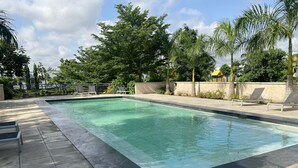 Una piscina rectangular con agua cristalina, rodeada por una terraza con baldosas y sillas de descanso.