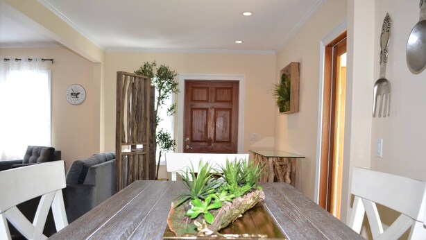 A dining area with a wooden table, white chairs, a potted plant, and a wooden door in the background. - Two fully independent units in a Duplex, with independent entrances. One Rent! (Key West)