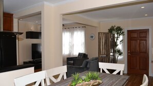 A dining area with a wooden table, white chairs, and a plant centerpiece. There is a kitchen area with a black refrigerator and a TV in the background. - Two fully independent units in a Duplex, with independent entrances. One Rent! (Key West)