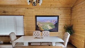 Una habitación con paneles de madera, una mesa de comedor blanca, sillas acolchadas y un cuadro enmarcado de un paisaje.