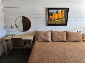 Une chambre à coucher comprenant un lit, un bureau, une chaise, un miroir rond et un tableau encadré accroché au mur.