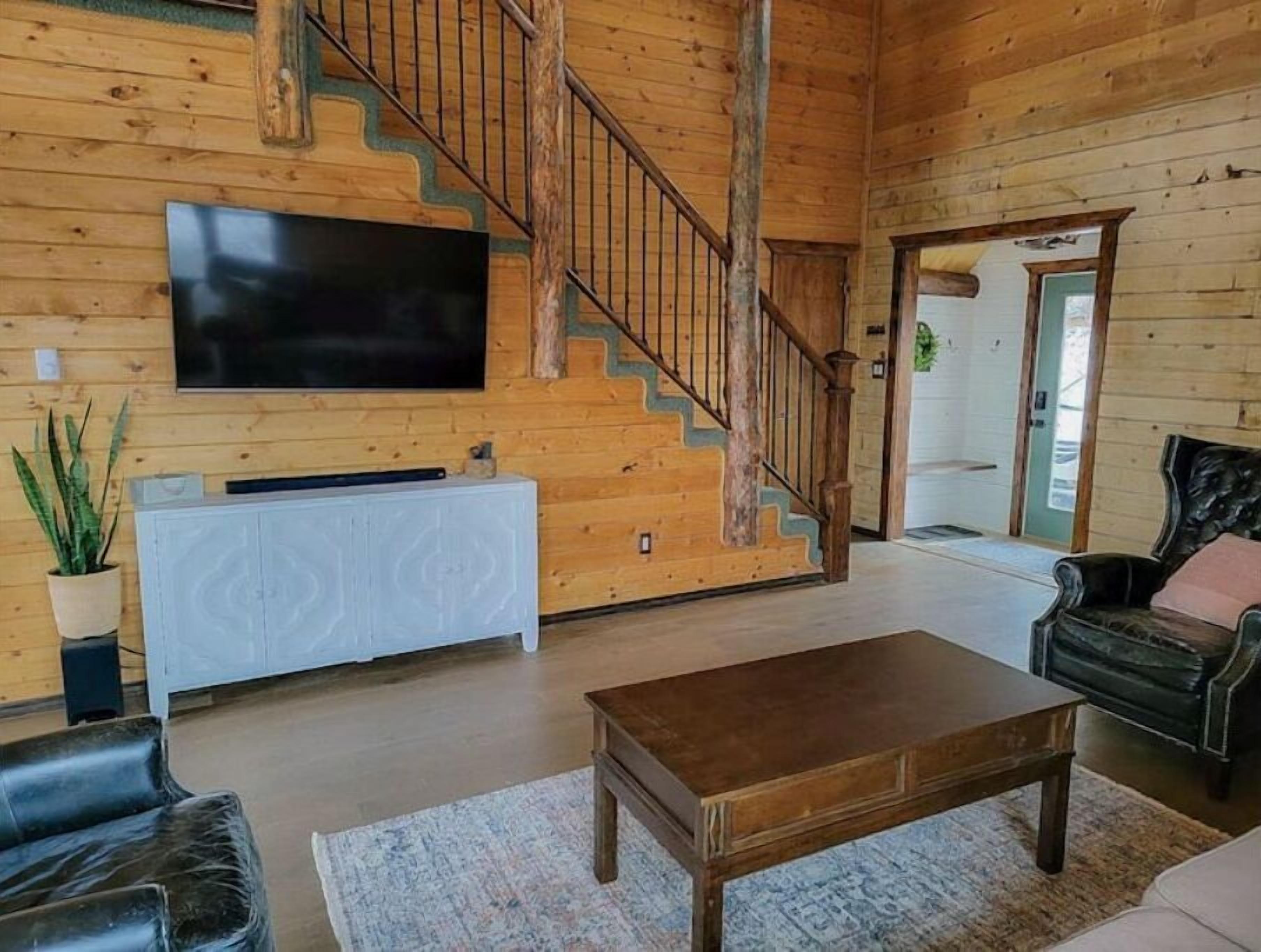 A wooden interior with a staircase, a flat-screen TV, a white cabinet, a coffee table, and a sofa.