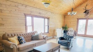 Un interior de cabaña acogedor con un sofá capitonado, un sillón de cuero, una mesa de centro de madera y una cabeza de venado montada en la pared.
