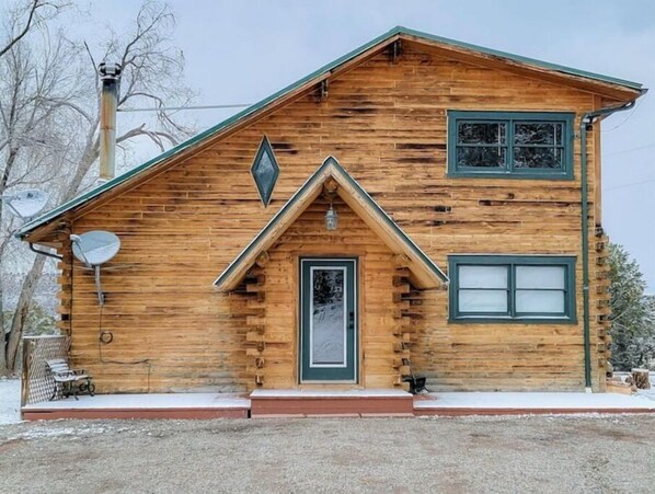 Une cabane en rondins avec un toit à pignon très incliné, une antenne parabolique et une porte d’entrée.