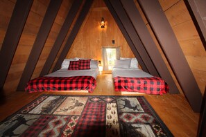 Un dormitorio acogedor en el ático, con dos camas, techo inclinado de madera y una alfombra estampada.