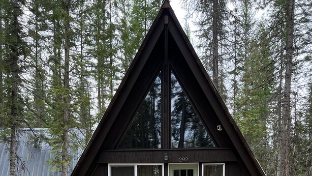 Eine schwarze Holzhütte mit grüner Tür, Fenstern und einem roten Schaukelstuhl davor.