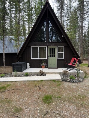 A black cabin with a green door, windows, and a red rocking chair outside. - Cozy Priest Lake Cabin (Priest Lake)