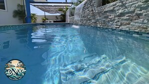 Une piscine à l’eau claire, un mur en pierre et un espace détente abrité.