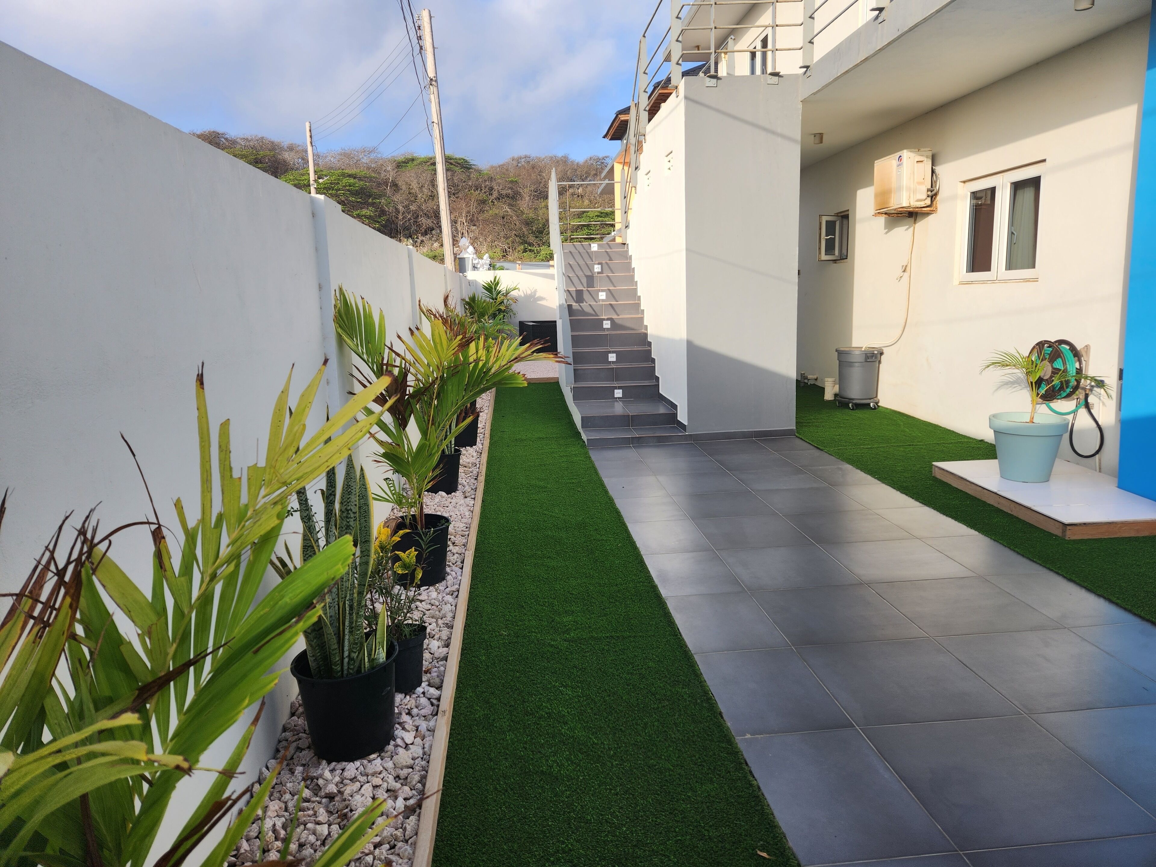 Un quartier résidentiel moderne doté d’un chemin pavé, de gazon synthétique et de plantes en pot.