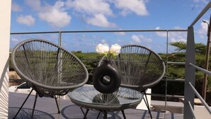 Un balcon avec deux fauteuils en osier et un vase rempli de fleurs blanches.