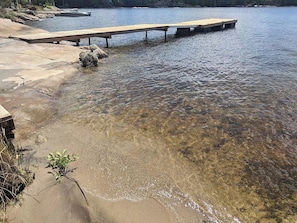 Ein klarer See mit einem hölzernen Steg, der sich ins Wasser erstreckt, umgeben von felsigem Ufer und klarem Wasser.