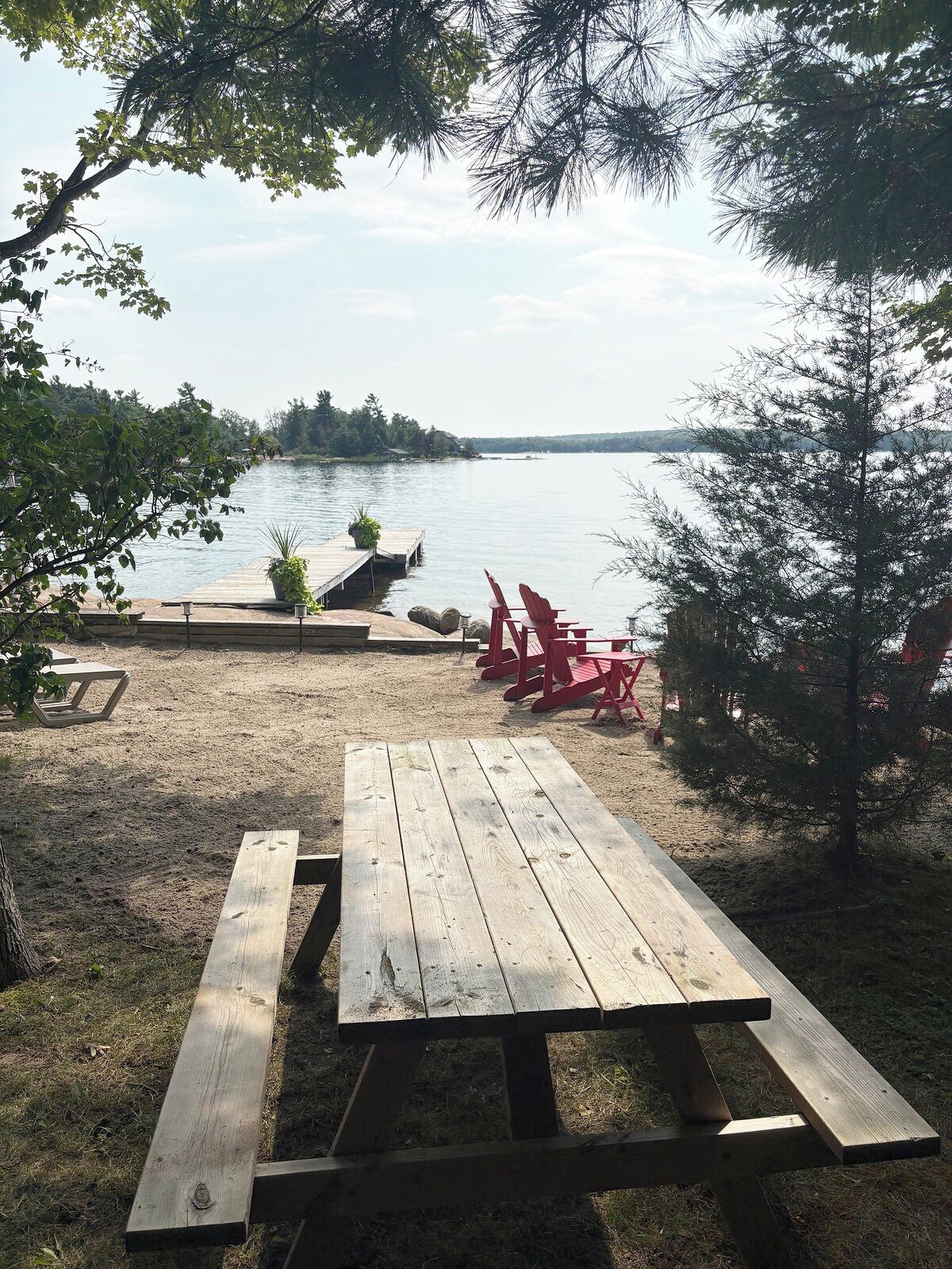 Een houten picknicktafel met banken, een klein steigerretje dat in een meer uitsteken, en rode stoelen.