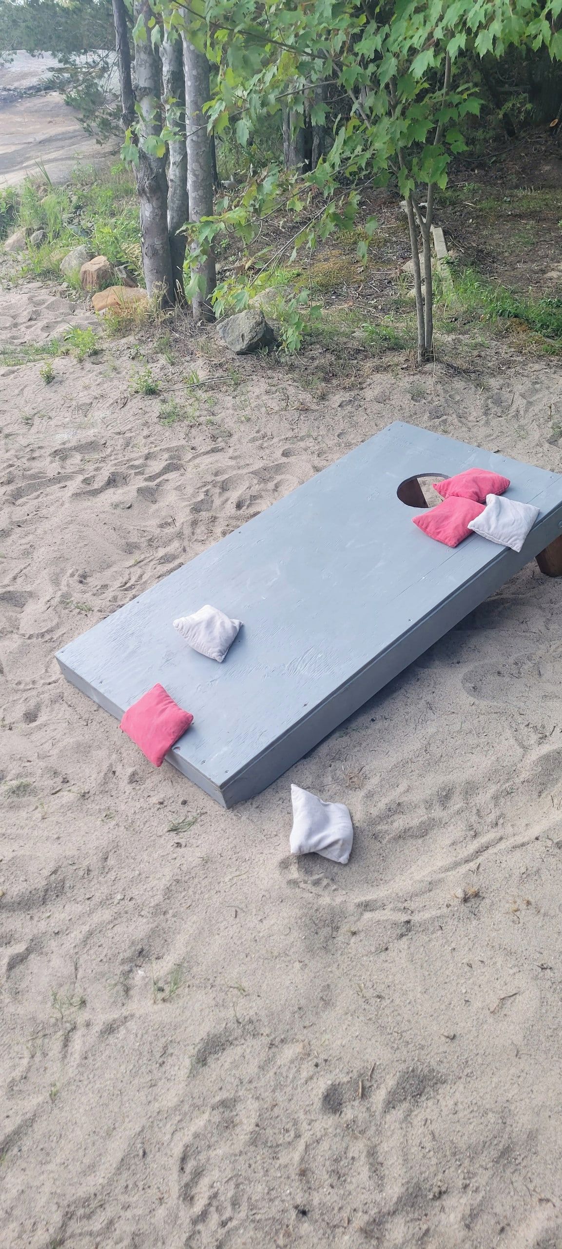 Un simple banc en bois, agrémenté de deux coussins, l’un rose et l’autre blanc, posé sur une surface sablonneuse.