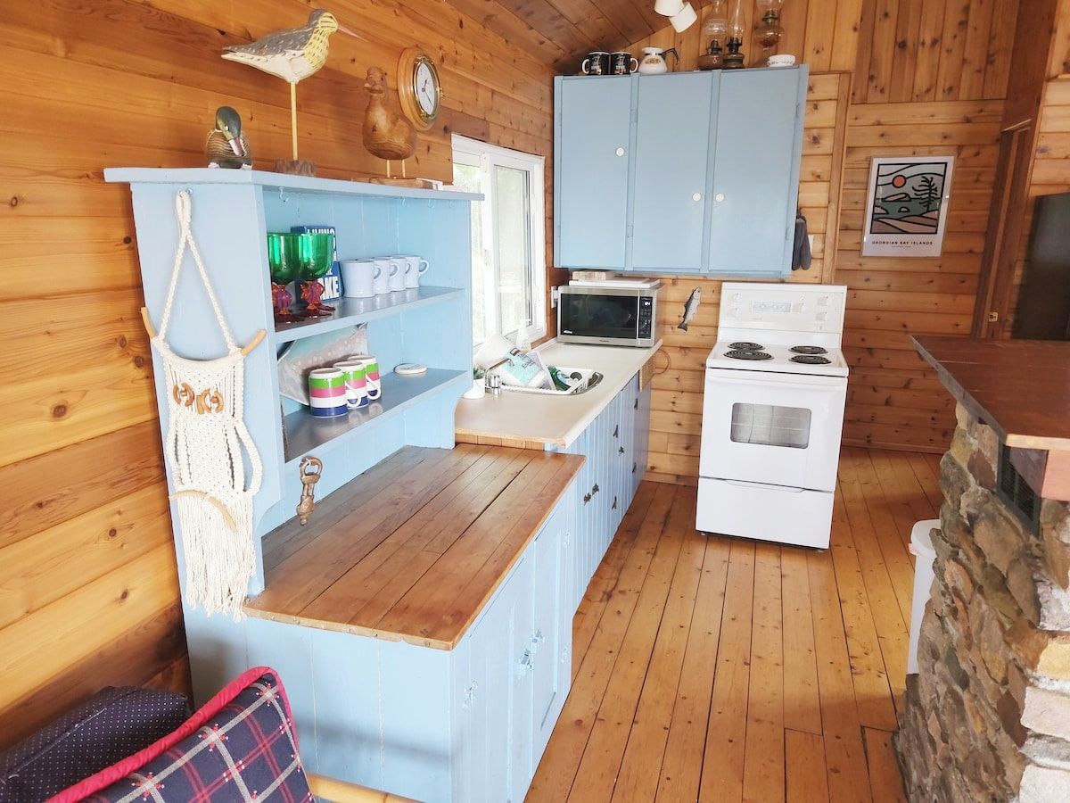 Une cuisine de taille réduite, équipée d’un four à micro-ondes, d’une cuisinière et de meubles de rangement bleus.