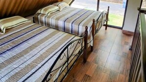 Une chambre avec un plafond en pente, un lit avec une literie à rayures et une vue sur un paysage verdoyant par une grande fenêtre.