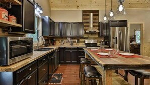 A modern kitchen with dark cabinetry, stainless steel appliances, and a wooden island with stools. - Chalet Bellaboo
Lic.#004390 (Ellijay)