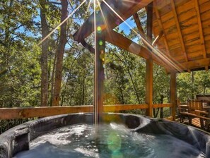 A hot tub in a wooden gazebo surrounded by trees.