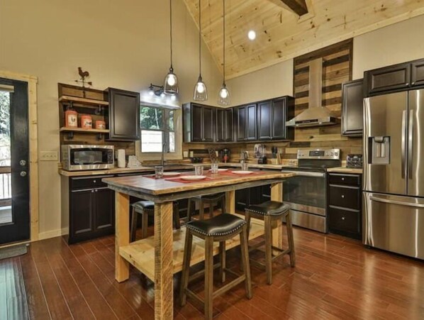 A modern kitchen with dark cabinets, stainless steel appliances, and a wooden island with stools. - Chalet Bellaboo
Lic.#004390 (Ellijay)