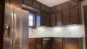 A kitchen with wooden cabinets, a stainless steel refrigerator, a dishwasher, and a marble countertop. - Walk to Beach Lake of Michigan, Lake Park, Eastside Milwaukee, Sleep 6, Parking (Milwaukee)