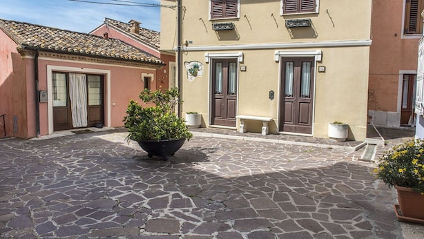 Een straat met cobblestones, gebouwen, een grote plantenbak met planten en een bankje.