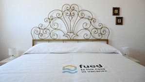 Een bed met een decoratief hoofdbord, wit beddengoed en twee ingelijste foto's aan de muur.