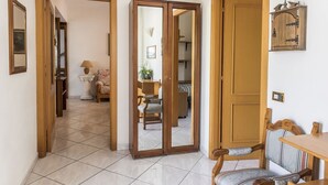 Um quarto com chão de azulejos, portas de madeira, uma mesa de jantar com cadeiras e um pequeno armário.