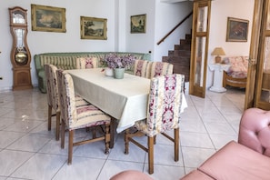 A dining room with a table set for four, surrounded by patterned chairs, a green sofa, and a staircase in the background.