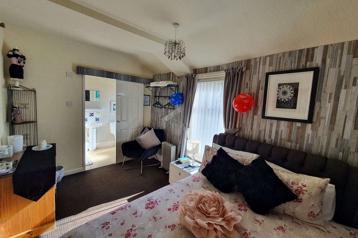 Ein Hotelzimmer mit Bett, Schreibtisch, Stuhl, Heizkörper, einem Fenster mit Vorhängen und einem Wandbild.