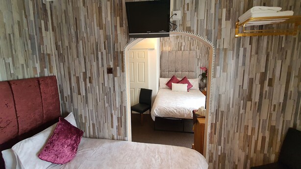 A hotel room with a large bed, a TV mounted on the wall, and a mirror above the bed. - Windsor House Hotel  (Blackpool)
