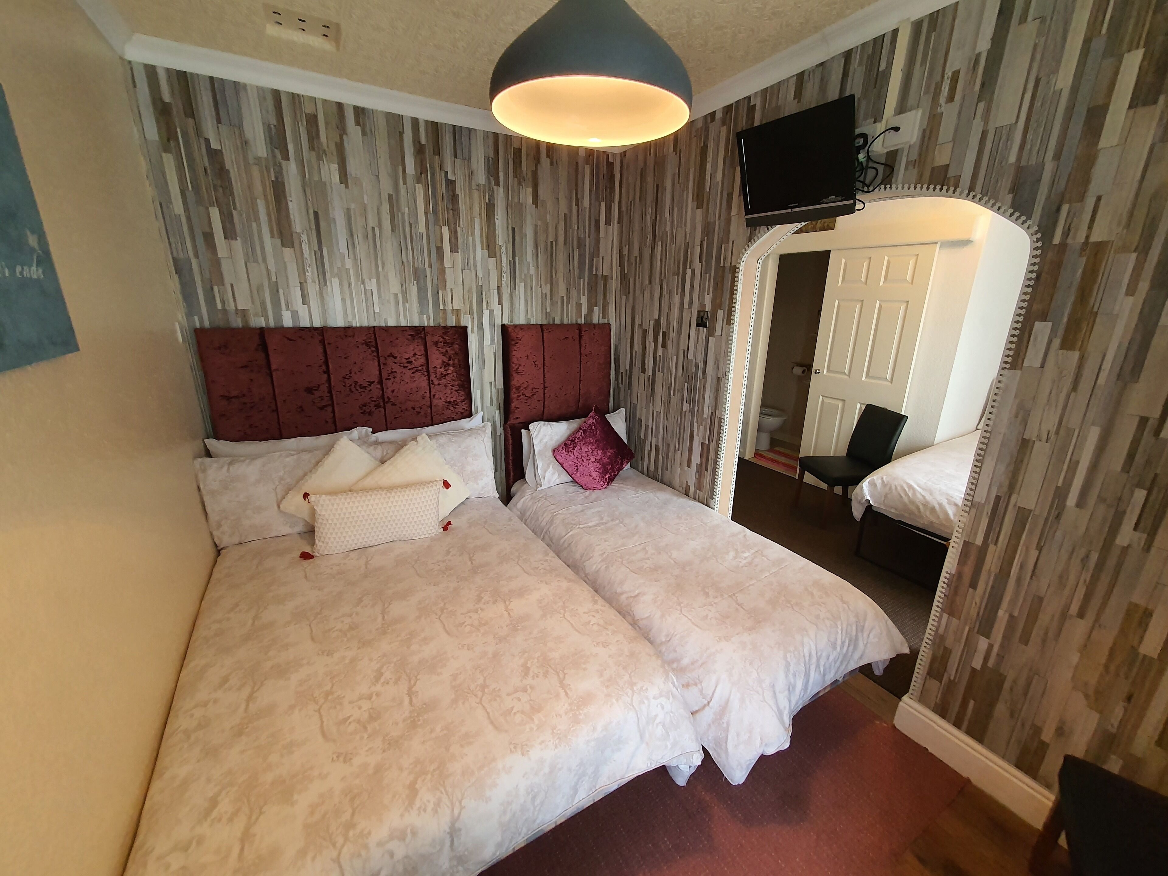 A double bed with a headboard, a bedside table, a mirror, and a television mounted on the wall.