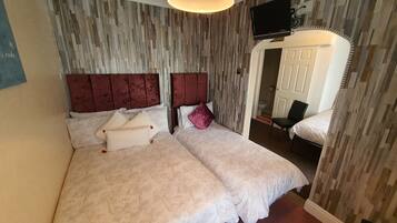 A double bed with a headboard, a bedside table, a mirror, and a television mounted on the wall.