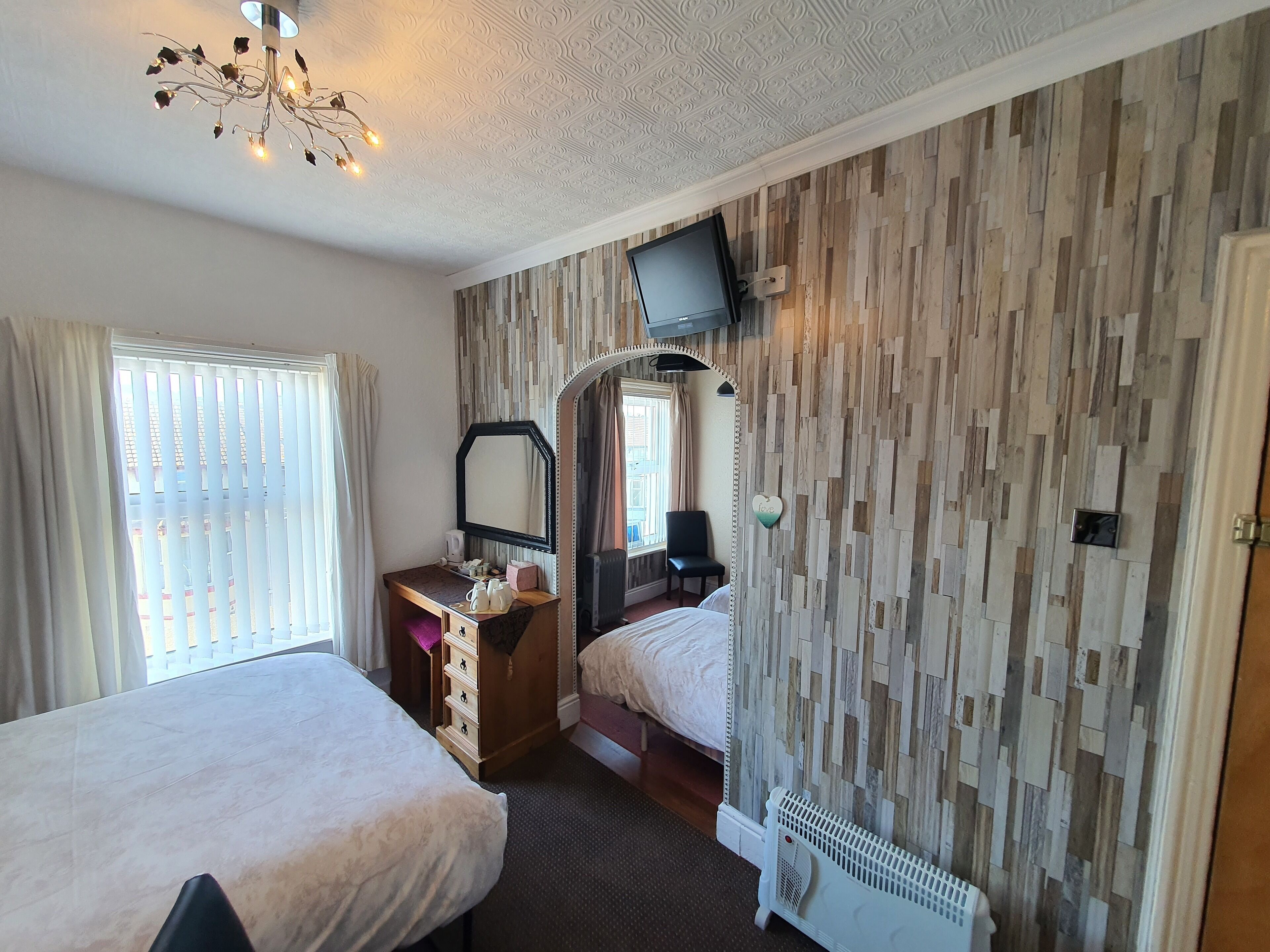 Habitación de hotel con dos camas, un escritorio con espejo, televisor montado en la pared y un radiador.