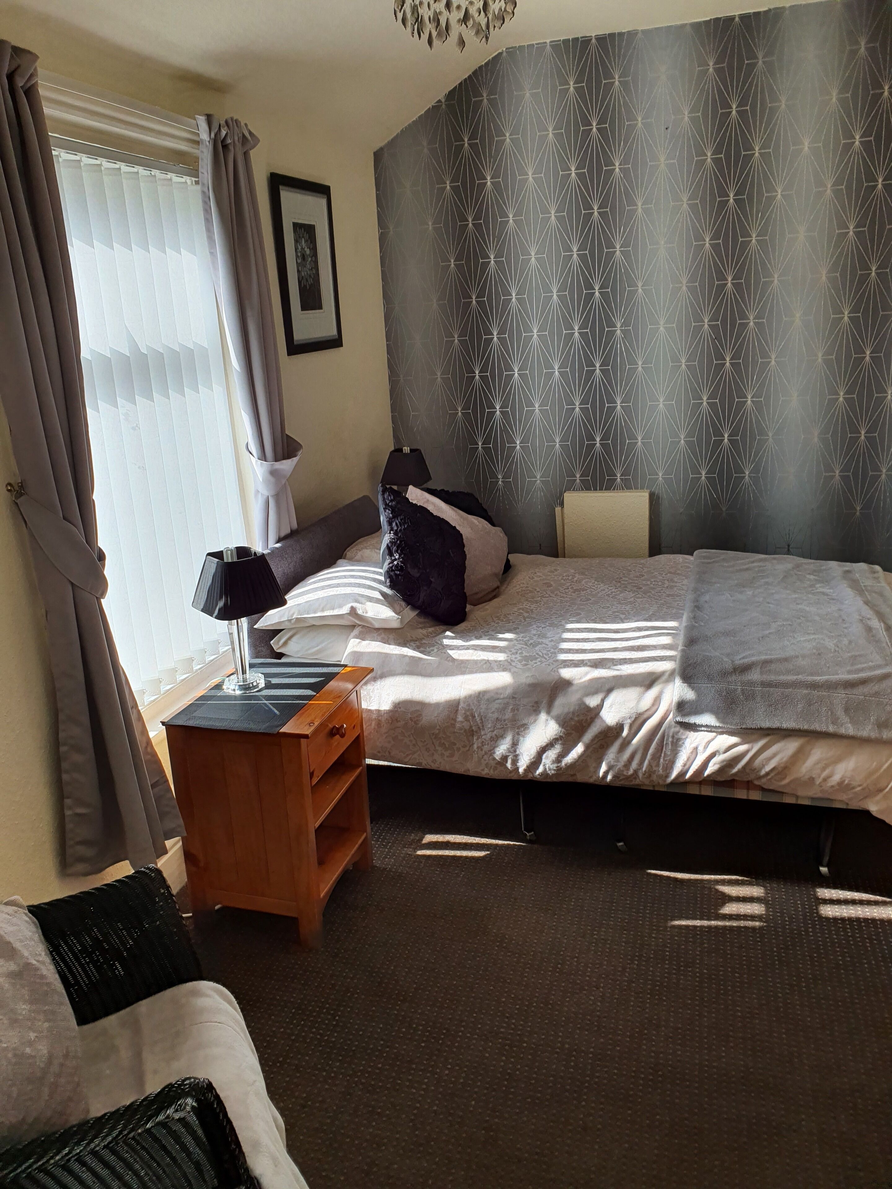 A bedroom with a bed, bedside table, lamp, and a patterned wall.