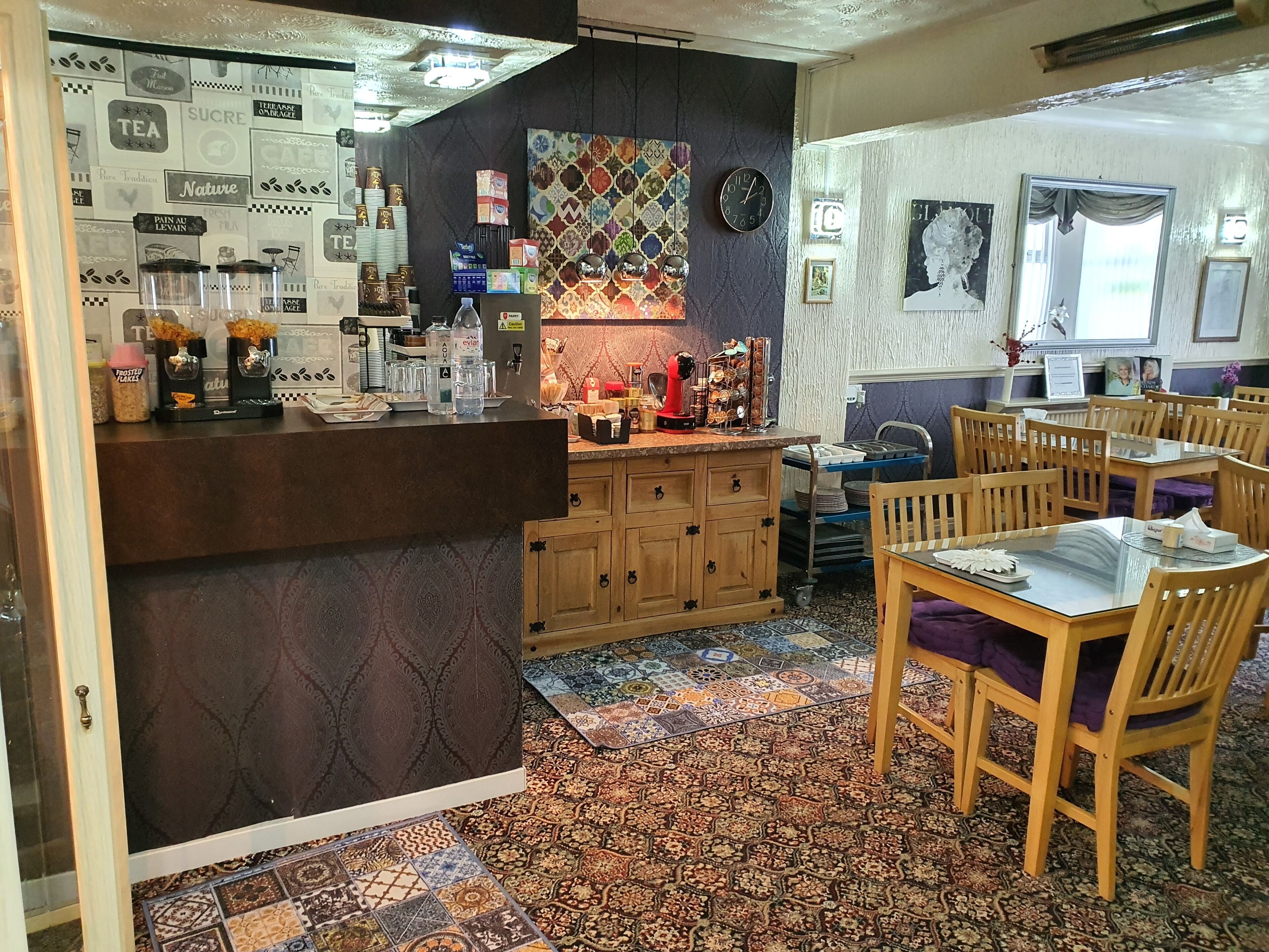 Een gezellig café met een toonbank, houten kasten, patroontegels en een eethoek met houten stoelen en tafels.