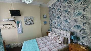 A bedroom with a bed, a dresser, a nightstand, a TV, and a chandelier.