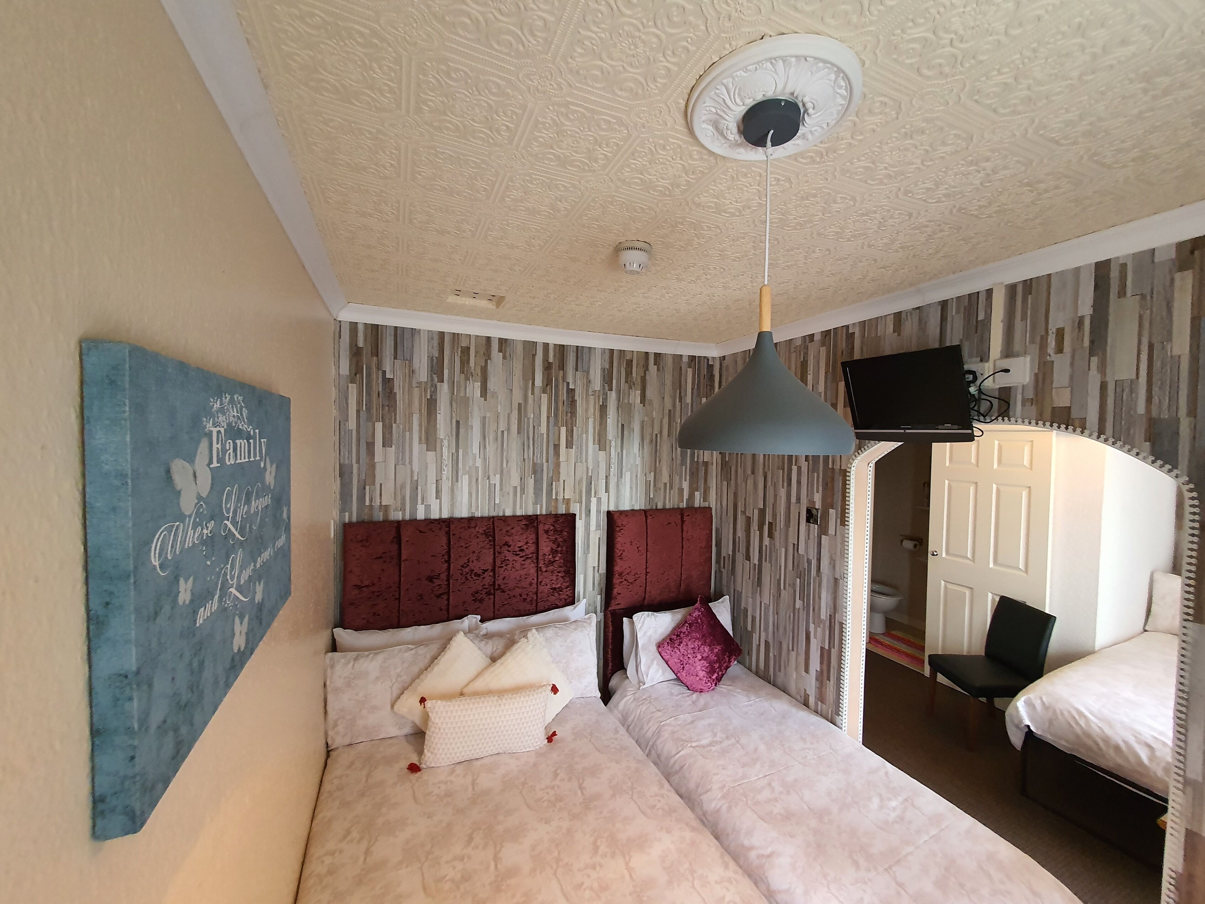 A bedroom with a large bed, a ceiling light, a mounted TV, and a wall-mounted artwork.