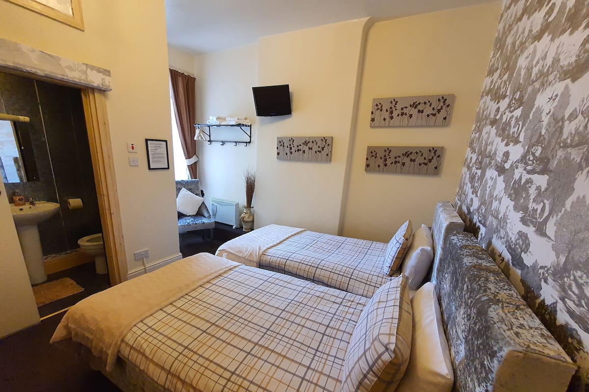 Ein Hotelzimmer mit zwei Betten, einem Badezimmer, einem Fernseher und Bildern an den Wänden.