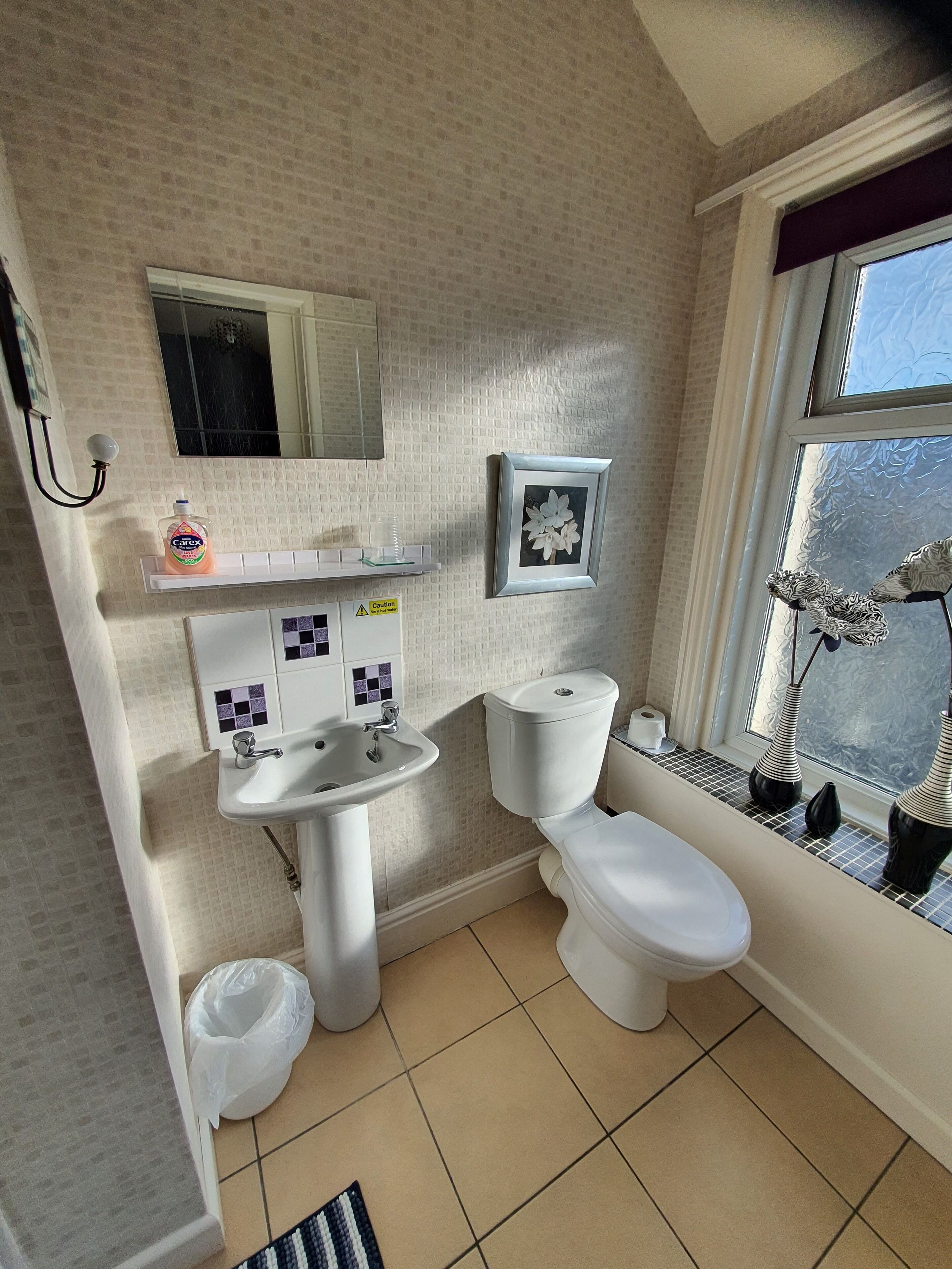A bathroom with a toilet, sink, and mirror. There is a window with a view of trees and a vase on the windowsill.