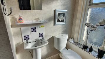 A bathroom with a toilet, sink, and mirror. There is a window with a view of trees and a vase on the windowsill.