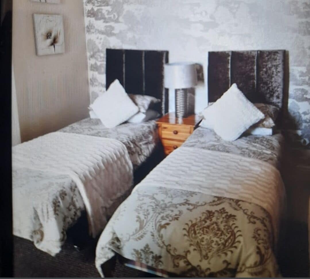 A double bed with a wooden headboard, a nightstand with a lamp, and a patterned bedspread.