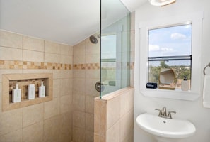 Un baño con ducha de vidrio, lavamanos y ventana con vistas.