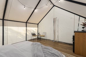 Une pièce aménagée comme une tente, avec un lit, une petite table et des chaises, ainsi qu’un meuble en bois.