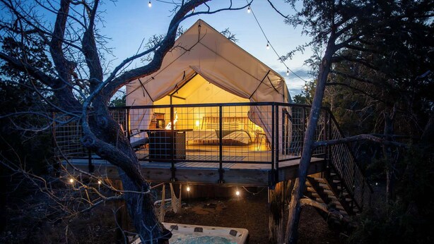 A treehouse with a hot tub and a bed, surrounded by trees and string lights.