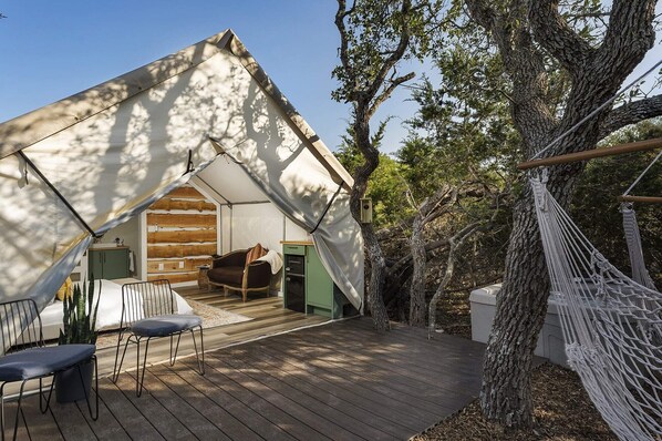A cozy, tent-like cabin with a wooden deck, a hammock, and a rustic interior.