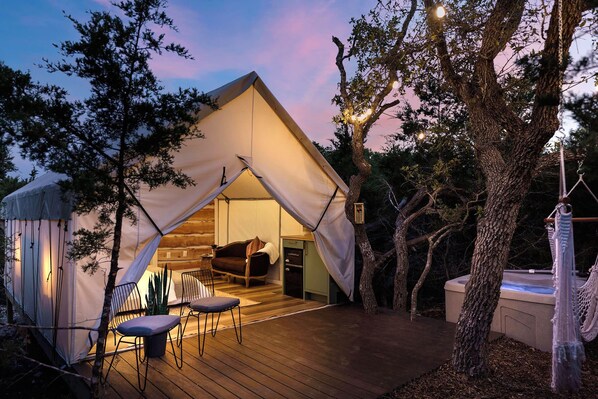 A tented accommodation with a hot tub, wooden deck, and a cozy seating area.
