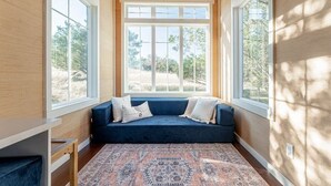 Une pièce avec un canapé bleu, un tapis à motifs et de grandes fenêtres donnant sur des arbres et un ciel dégagé.