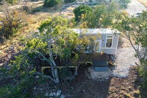 Eine kleine, eingeschossige Holzhütte mit einem eingezäunten Hof, umgeben von Bäumen und trockenem Gras.