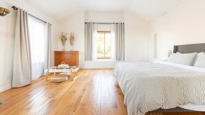 Ein Schlafzimmer mit Holzboden, einem Bett mit gestreifter Bettdecke, einem Schminktisch und einem Fenster mit Vorhängen.
