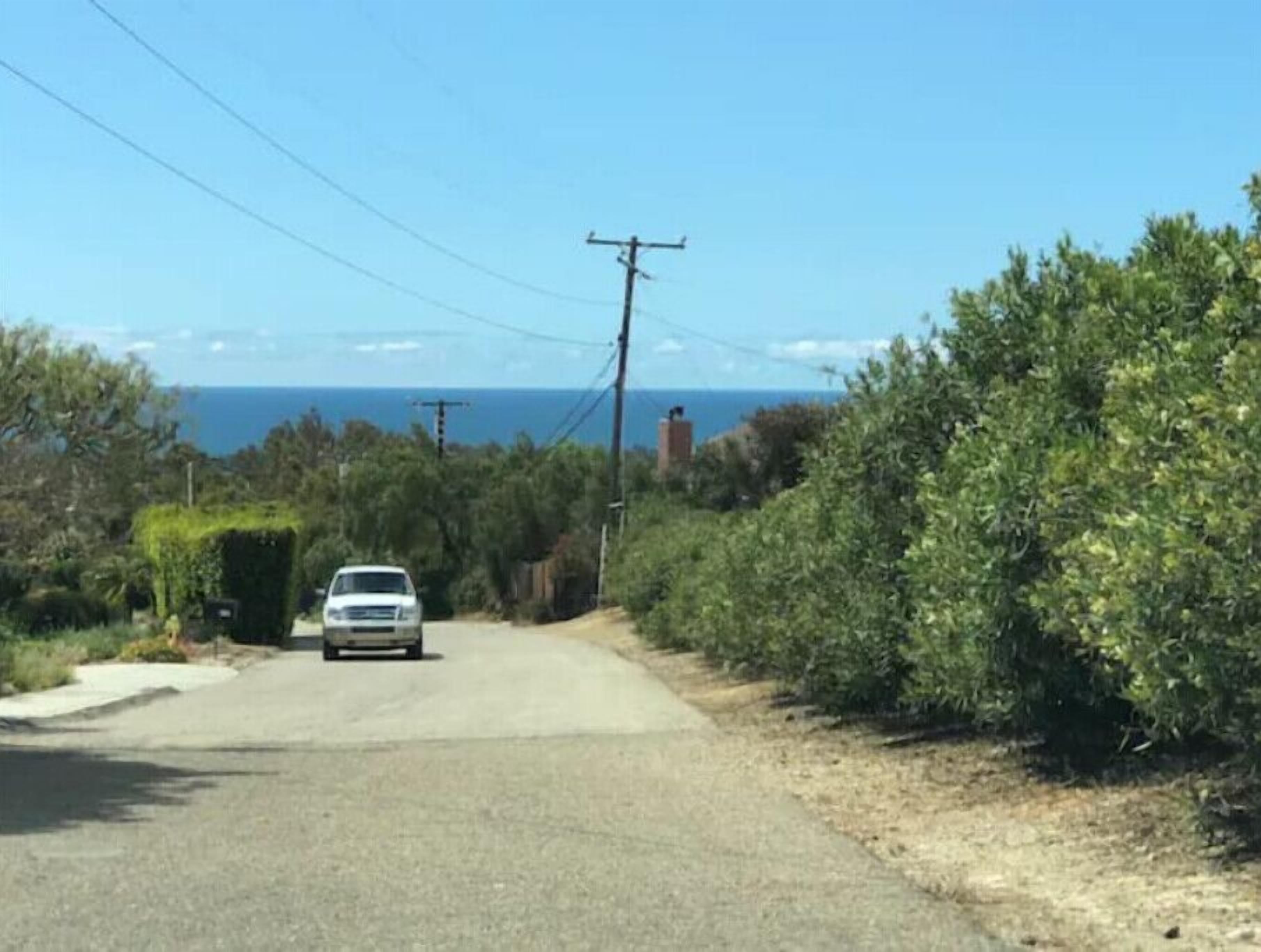 Une route bordée d’arbres, avec une voiture, et offrant une vue sur la mer.