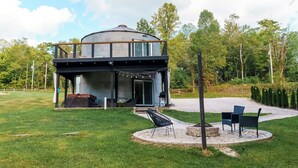A modern two-story house with a circular structure, a covered outdoor seating area, and a well-maintained lawn. - Restored Grain Bin with Hot Tub, King Bed, Vending Machine. Dog-friendly! (Rockbridge)